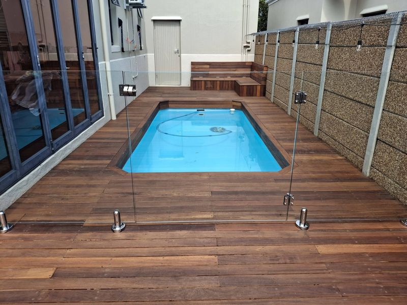 A plunge pool set into a new reddish-brown balau timber deck, with a built-in timber bench and a frameless glass fence.