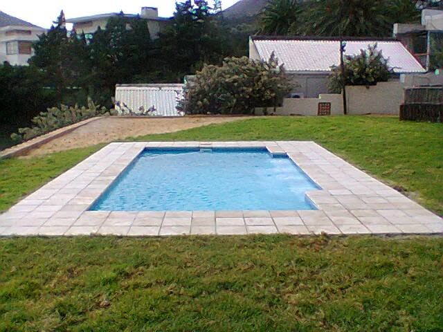 A rectangular pool with pale stone coping, set into a green lawn with mountains behind.