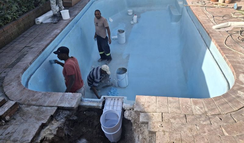 Three workers resurfacing an empty pool in pale blue, with a new skimmer box being fitted at the edge.