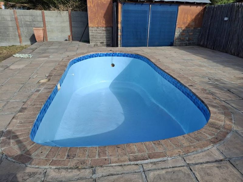 An empty kidney-shaped pool, freshly resurfaced in blue, with a band of dark blue mosaic tiles at the waterline and a brick coping.