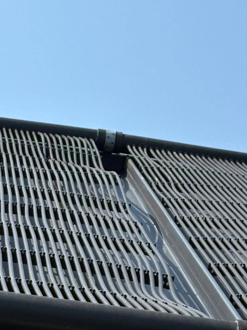 Black solar pool-heating mats laid across a roof under a clear blue sky.
